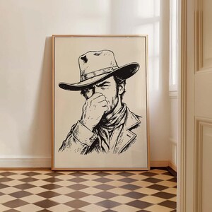 Pode incluir: Uma impressão artística de linhas em preto e branco emoldurada, apresentando o retrato de uma pessoa usando um chapéu de cowboy de aba larga e um lenço no pescoço, com uma mão levantada em direção ao rosto. A ilustração é em estilo de esboço.