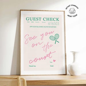 May include: A framed print featuring a guest check design with the text "GUEST CHECK" and "See you on the court." The design includes tennis rackets and a heart. The print is displayed on a wooden surface.