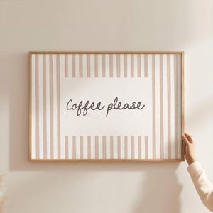 Könnte beinhalten: Ein rechteckiges Wandbild in einem hellen Holzrahmen mit einem weißen Mittelfeld, auf dem der Text "Coffee please" in dunkelgrauer Schreibschrift steht, umrahmt von vertikalen beigen und weißen Streifen an allen Seiten.