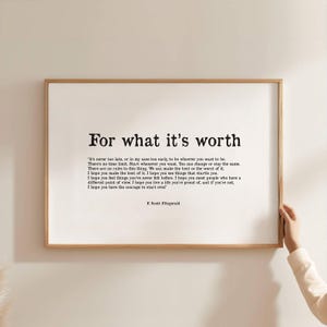 Può includere: Una stampa incorniciata con il testo "For what it's worth" e una citazione di F. Scott Fitzgerald. La stampa ha uno sfondo bianco e una cornice in legno marrone chiaro. Una mano tiene la cornice.