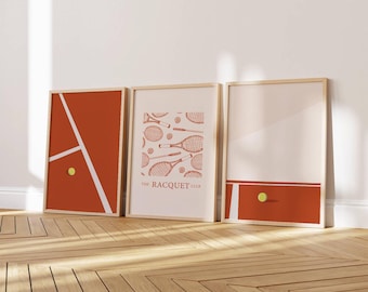May include: Three framed tennis-themed prints. The prints feature a tennis court design, tennis rackets, and a tennis ball. The color palette includes shades of orange, white, and beige, with wooden frames.