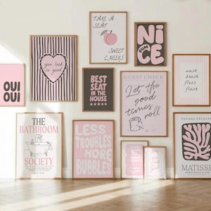 Pode incluir: Uma galeria de parede com doze impressões artísticas emolduradas, apresentando uma paleta de cores rosa e preta. As impressões incluem tipografia, ilustrações de um pêssego, uma banheira, papel higiénico e formas abstratas em molduras de madeira.