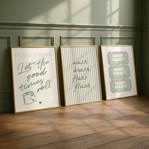 Three sage green and pastel mint printable bathroom wall art posters leaning against a wall, featuring a funny toilet print with “let the good times roll,” a striped wash brush floss flush sign, and a retro shower karaoke ticket-style design, styled as trendy aesthetic restroom decor.