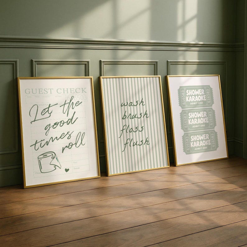 Three sage green and pastel mint printable bathroom wall art posters leaning against a wall, featuring a funny toilet print with “let the good times roll,” a striped wash brush floss flush sign, and a retro shower karaoke ticket-style design, styled as trendy aesthetic restroom decor.