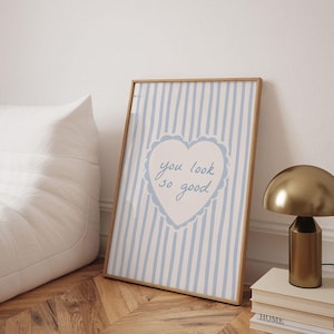 May include: A rectangular framed print featuring a light blue and white vertical striped background. In the center, a white heart with a scalloped blue border contains the handwritten blue text that reads, you look so good.