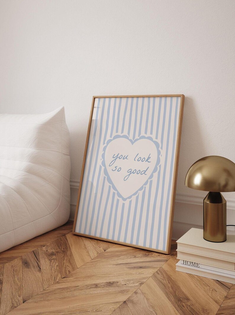 May include: A rectangular framed print featuring a light blue and white vertical striped background. In the center, a white heart with a scalloped blue border contains the handwritten blue text that reads, you look so good.