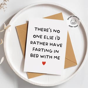 May include: A white greeting card with the text "THERE'S NO ONE ELSE I'D RATHER HAVE FARTING IN BED WITH ME" and a red heart, placed on a brown envelope. The card and envelope are on a white tray.