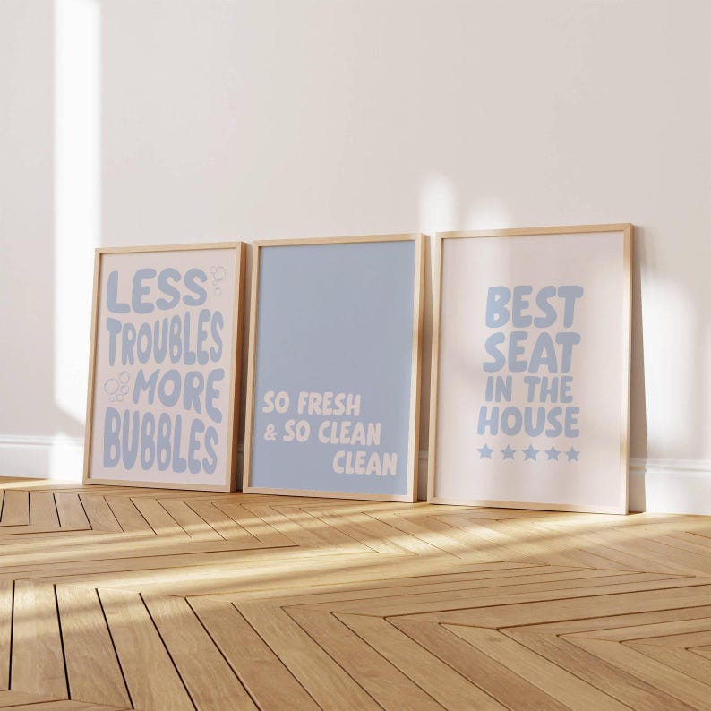Images shows 3 funny bathroom prints with wood frames, displaying text-based designs in pastel blue & white. The artwork includes phrases such as "Best Seat In The House" and "So Fresh & So So Clean", suitable for bathroom decor.