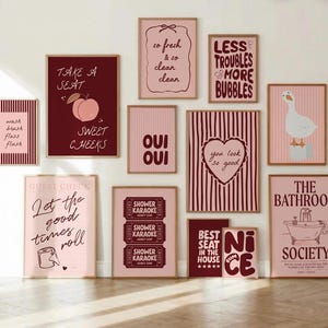 May include: A collection of framed wall art with various bathroom-themed quotes and illustrations. The color palette includes shades of pink, burgundy, and white. The art pieces feature phrases like "Sweet Cheeks" and "The Bathroom Society."