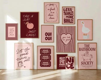 May include: A collection of framed wall art with various bathroom-themed quotes and illustrations. The color palette includes shades of pink, burgundy, and white. The art pieces feature phrases like "Sweet Cheeks" and "The Bathroom Society."