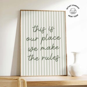 Może przedstawiać: Oprawiony wydruk z jasnozielono-białym paskowanym tłem i napisem "this is our place we make the rules" w kursywie. Biały wazon stoi na drewnianej powierzchni.