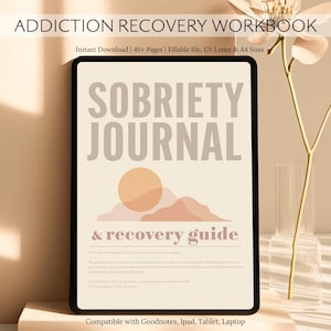 May include: A digital sobriety journal and recovery guide displayed on a tablet. The journal features the words "Sobriety Journal & Recovery Guide" with a sun and mountain graphic. The tablet is on a light-colored surface.