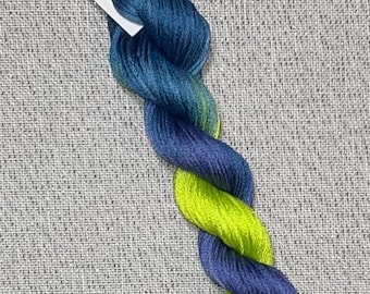 May include: A skein of hand-dyed cotton embroidery floss in shades of blue and green. The floss is twisted and has a gradient effect. The label reads "Dyeing for Cross Stitch" and "Hand Dyed Fabric and Floss".