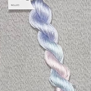 Puede incluir: Un ovillo de hilo de algodón teñido a mano en tonos pastel de azul y rosa, retorcido en forma de cuerda. Una etiqueta blanca con el texto "Dyeing for Cross Stitch" y la dirección del sitio web está adjunta.