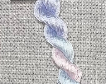 May include: A skein of hand-dyed cotton floss in pastel shades of blue and pink, twisted into a rope-like shape. A white tag with the text "Dyeing for Cross Stitch" and website address is attached.