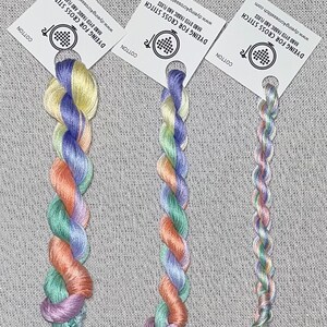 May include: Three skeins of hand-dyed embroidery floss in a rainbow colour gradient. The floss is wound on white cards with the text "Dyeing for Cross Stitch" and a website address.