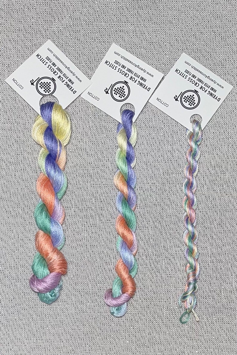 May include: Three skeins of hand-dyed embroidery floss in a rainbow colour gradient. The floss is wound on white cards with the text "Dyeing for Cross Stitch" and a website address.