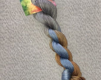 May include: A skein of hand-dyed cotton embroidery floss in shades of gray, blue, and brown. The floss is labeled "Dyeing for Cross Stitch Cotton - hand dyed fibers".