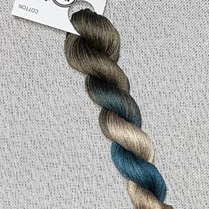 May include: A twisted skein of hand-dyed cotton floss in shades of blue, brown, and tan, with a white tag that reads "Dyeing for Cross Stitch" and "Cotton."
