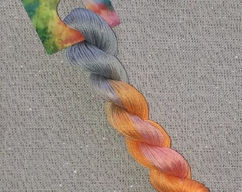 May include: A skein of hand-dyed embroidery floss in shades of blue, orange, and pink. The floss is labeled "Dyeing for Cross Stitch Cotton - hand dyed floss".