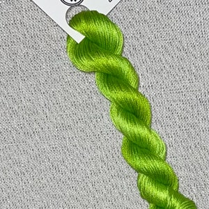 May include: A skein of bright green hand-dyed cotton embroidery floss for cross stitch. The floss is labeled "Dyeing for Cross Stitch" and "Hand Dyed Fabric and Floss".