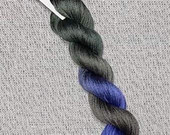 May include: A skein of hand-dyed cotton embroidery floss in shades of dark green, black, and blue. The floss is labeled "Dyeing for Cross Stitch" and "Hand Dyed Fabric and Floss".