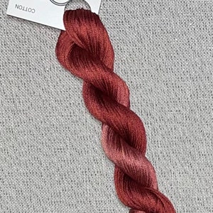 May include: A skein of hand-dyed embroidery floss in shades of red and pink. The floss is wound around a white card with the text "Dyeing For Cross Stitch" and "Hand Dyed Fabric and Floss" printed on it. The card also includes the website address "www.dyeing4crossstitch.com".