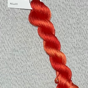 Puede incluir: Un ovillo de hilo de bordar teñido a mano en tonos naranja y rojo. El hilo está etiquetado con "Dyeing for Cross Stitch" y "Hand Dyed Fabric and Floss" con la dirección del sitio web "www.dyeing4crossstitch.com". El hilo está etiquetado como "Cotton".