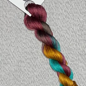 May include: A skein of hand-dyed cotton embroidery floss in shades of burgundy, teal, gold, and brown. The floss is labeled "Dyeing for Cross Stitch" and "Hand Dyed Fabric and Floss".