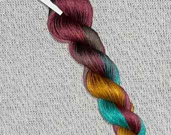 May include: A skein of hand-dyed cotton embroidery floss in shades of burgundy, teal, gold, and brown. The floss is labeled "Dyeing for Cross Stitch" and "Hand Dyed Fabric and Floss".