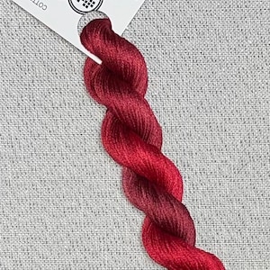 May include: A skein of hand-dyed cotton floss in shades of red and burgundy, perfect for cross stitch. The floss is attached to a white tag with the text "Dyeing for Cross Stitch" and a website address.