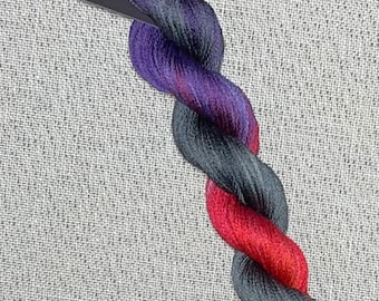 May include: A skein of hand-dyed cotton embroidery floss in shades of purple, red, orange, and gray. The floss is labeled "Dyeing for Cross Stitch Hand Dyed Fabric and Floss Cotton".
