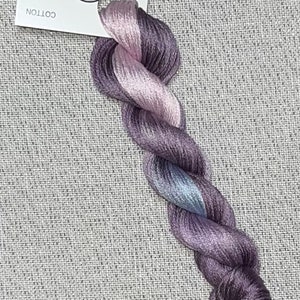 May include: A skein of hand-dyed cotton floss in shades of purple, lavender, and silver. The floss is twisted and has a tag that reads "Dyeing for Cross Stitch" and "Hand Dyed Fabric and Floss."