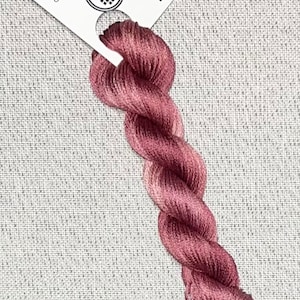May include: A skein of hand-dyed embroidery floss in a gradient of pink and red shades. The floss is labeled "Dyeing for Cross Stitch" and "Hand Dyed Fadic and Floss" with the website address "www.dyeing4crossstitch.com".