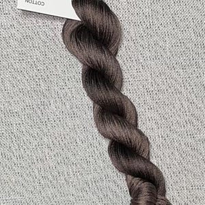 May include: A skein of dark brown cotton embroidery floss. The floss is hand-dyed and is labeled "Dyeing for Cross Stitch" with the website address "www.dyeingforcrossstitch.com".