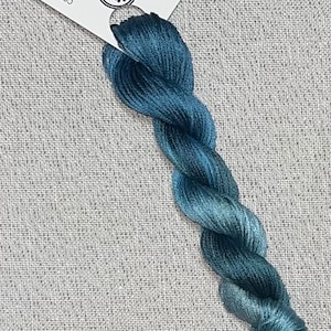 May include: A skein of hand-dyed cotton embroidery floss in shades of blue and green. The floss is labeled "Dyeing For Cross Stitch" and "Hand Dyed Fabric and Floss".