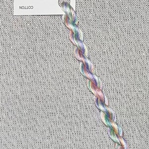 May include: A skein of hand-dyed cotton embroidery floss in shades of green, pink, and purple. The floss is wrapped around a white card with the text "Dyeing For Cross Stitch" and "Hand Dyed Fabric and Floss" and the website address "www.dyeing4crossstitch.com".