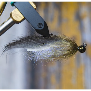 May include: A close-up of a fly fishing lure with a black, white, and green feather body and a gold bead head.