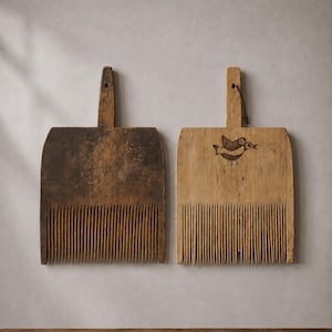 Puede incluir: Dos peines de lana rectangulares de madera con dientes verticales largos y finos. El peine izquierdo es de color marrón oscuro con acabado desgastado. El derecho es de color tostado claro, tiene un dibujo de un pájaro y una tira de cuero.
