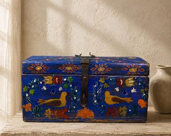 May include: A rectangular wooden chest painted in a vibrant blue, featuring hand-painted floral motifs and two yellow birds on the front panel. The lid is secured with a dark metal latch and hinge hardware, showcasing a weathered finish throughout.