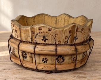May include: A round wooden bowl with a scalloped top edge, featuring a light tan finish and dark brown stamped floral and cross patterns. The exterior is reinforced with two horizontal wooden bands and a dark brown twisted wire cage structure.