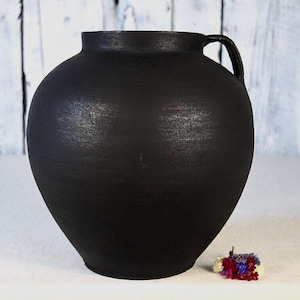 May include: A white ceramic mug with a black handle and the text "But First, Coffee" in a black, bold font. The mug is sitting on a wooden surface. The mug is 4 inches tall.