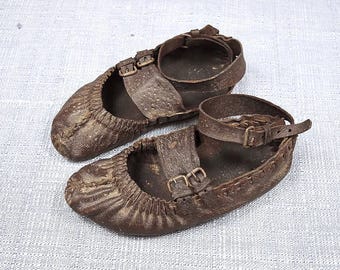 May include: A pair of brown leather sandals with ankle straps and buckle closures. The sandals have a rounded toe and a textured appearance, suggesting a vintage or handcrafted style. The leather appears worn, adding to their rustic charm.