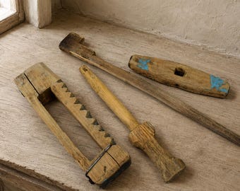 May include: Three vintage wooden tools with weathered textures. One tool features a serrated edge and a metal bracket, another is a long rod with a shaped handle, and the third is a flat, elongated piece with blue paint accents on both ends.