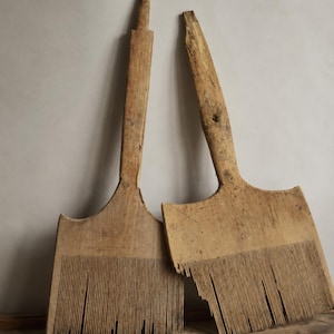 May include: Two antique wooden flax combs with long, flat handles and numerous thin, vertical wooden teeth. The light brown wood shows a weathered, textured grain with visible signs of age, wear, and natural imperfections across the surfaces.