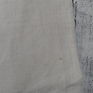Puede incluir: Un trozo de tela de color beige claro con una textura tejida visible y una peque&ntilde;a mancha marr&oacute;n sutil en la superficie. El material parece ser un tejido de fibra natural con un patr&oacute;n de tejido consistente en toda la secci&oacute;n visible.