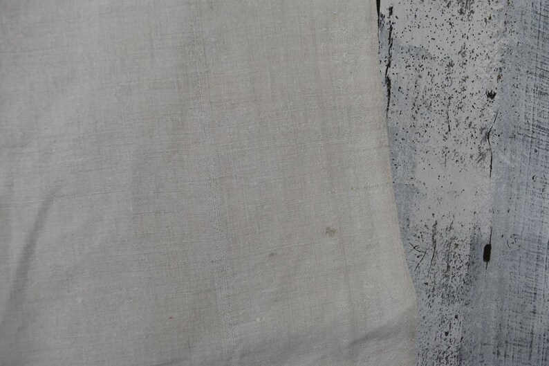 Puede incluir: Un trozo de tela de color beige claro con una textura tejida visible y una peque&ntilde;a mancha marr&oacute;n sutil en la superficie. El material parece ser un tejido de fibra natural con un patr&oacute;n de tejido consistente en toda la secci&oacute;n visible.