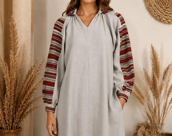 May include: A light gray knee-length dress with a V-neckline and long sleeves. The sleeves feature horizontal stripes in shades of red, green, and white. The collar and sleeve cuffs are accented with a detailed, multi-colored embroidered pattern.