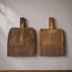 Puede incluir: Dos peines de lino de madera antiguos con dientes verticales largos y finos y un mango rectangular con un pequeño orificio en la parte superior. La madera muestra una pátina marrón oscura desgastada con signos visibles de uso y vetas.