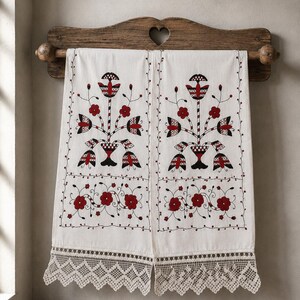 Puede incluir: Dos toallas rectangulares de color blanco roto con intrincados patrones de bordado floral en rojo y negro. Cada toalla muestra un motivo botánico central y un borde inferior de flores rojas, acabado con un ancho encaje de ganchillo crema.